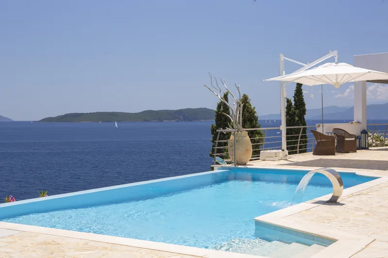 Infinity pool with a water spout, driftwood in a tall urn and a white parasol, the islands beyond