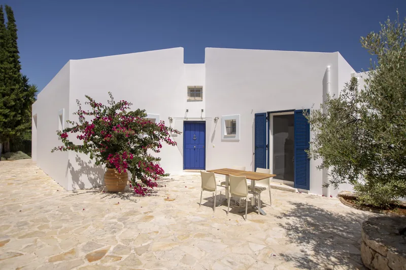 Whitewashed house with a cobalt blue door and shutters, bougainvillea in a terracotta urn and a teak table on the flagstone courtyard