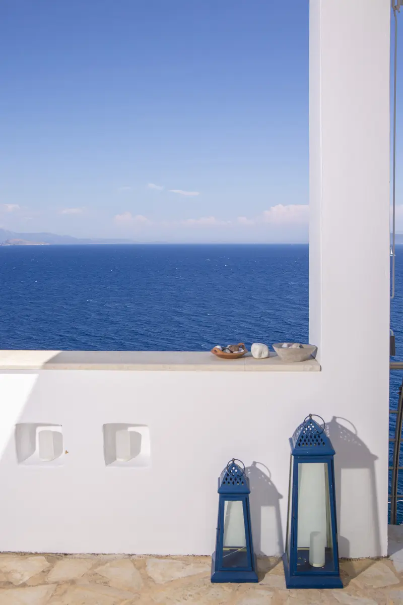 White parapet framing the deep blue sea, with pebble bowls and indigo lanterns on the stone terrace