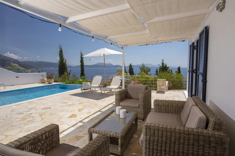 Rattan lounge under the pergola with string lights, the pool and sea beyond