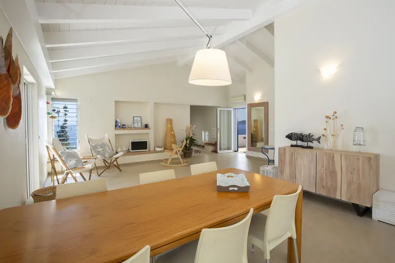 Long dining table under a beamed ceiling with doors open to the terrace